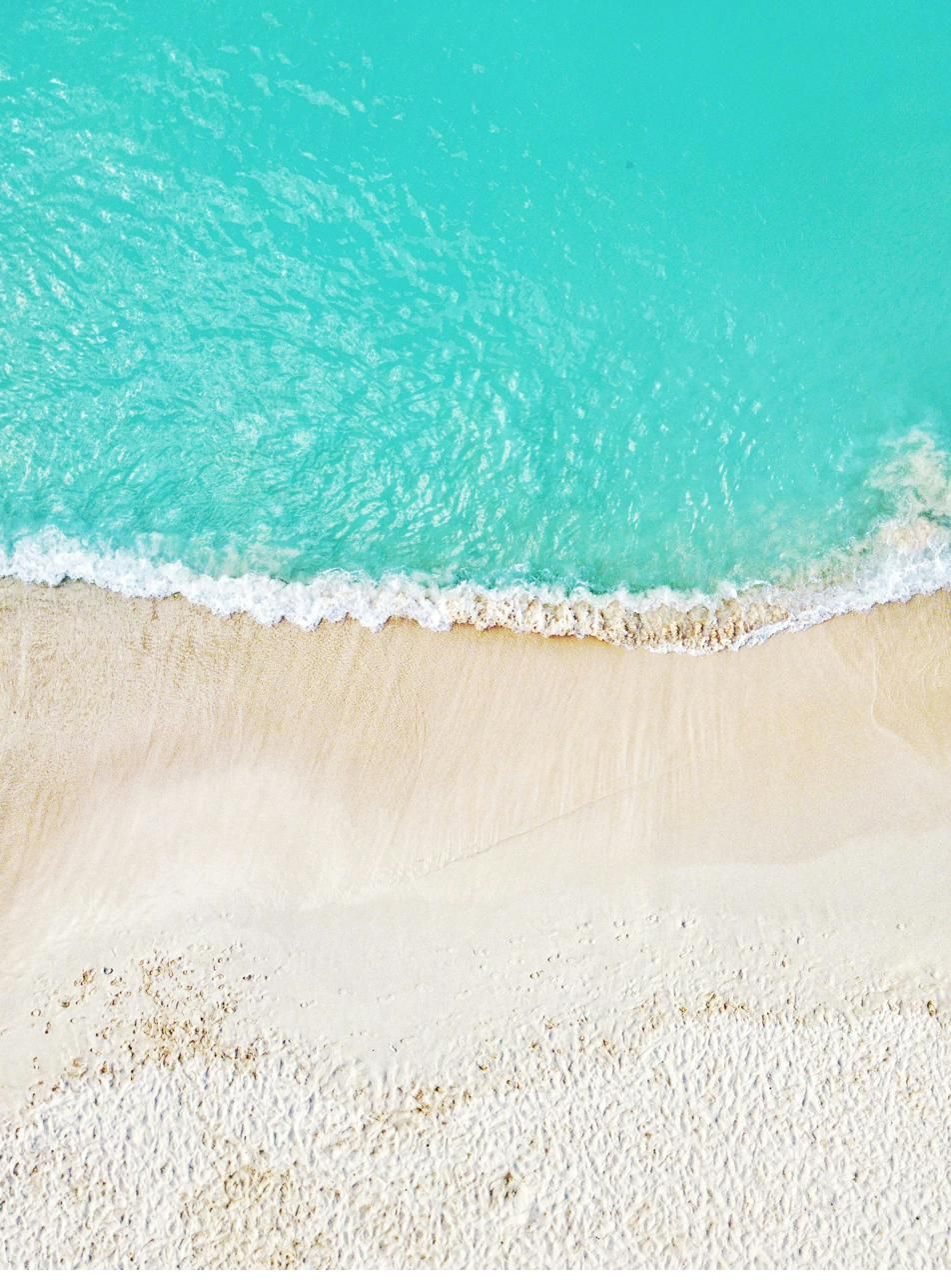 Turquoise water meeting a wide band of white sand on Seven Mile Beach, Grand Cayman, seen from above