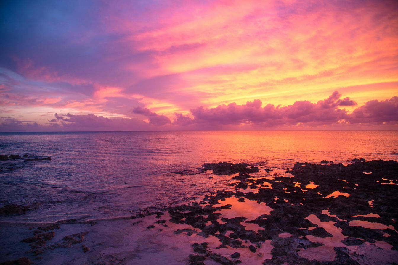 A pink and gold sunset over the ironshore and open water on Grand Cayman